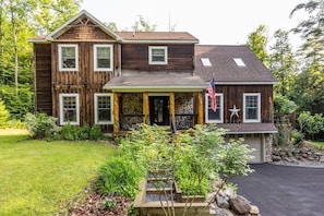 A two-story wooden house with a stone foundation, a front porch, and a garage.