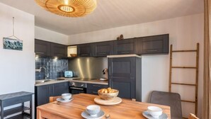 A modern kitchen with dark cabinets, a wooden dining table, and a hanging light fixture. - Ortal Océan by Interhome (Lacanau)