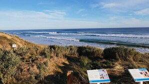 Een kustgezicht met een zandstrand, golven in de oceaan en wat begroeiing.