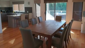 Een ruime eethoek met een grote houten tafel en zes stoelen, een keuken met moderne apparatuur, en grote ramen met uitzicht op de omgeving.