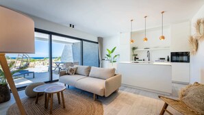 Un salon moderne avec un canapé, une petite table et une vue sur l’océan grâce à de grandes fenêtres.