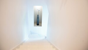 Unes escales estretes amb un petit finestral a dalt, que condueixen a una habitació on hi ha un ram de flors blaves fosques en un moble.