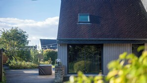 Una casa moderna amb un teulat inclinat, una zona d'estar exterior coberta i un gran vidre d'entrada.
