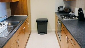 A kitchen with wooden cabinets, a black trash bin, a stove, and a sink. - No 2 - Modern 2 Bed Apartment, Close to Gla Airport & M8 (Paisley)