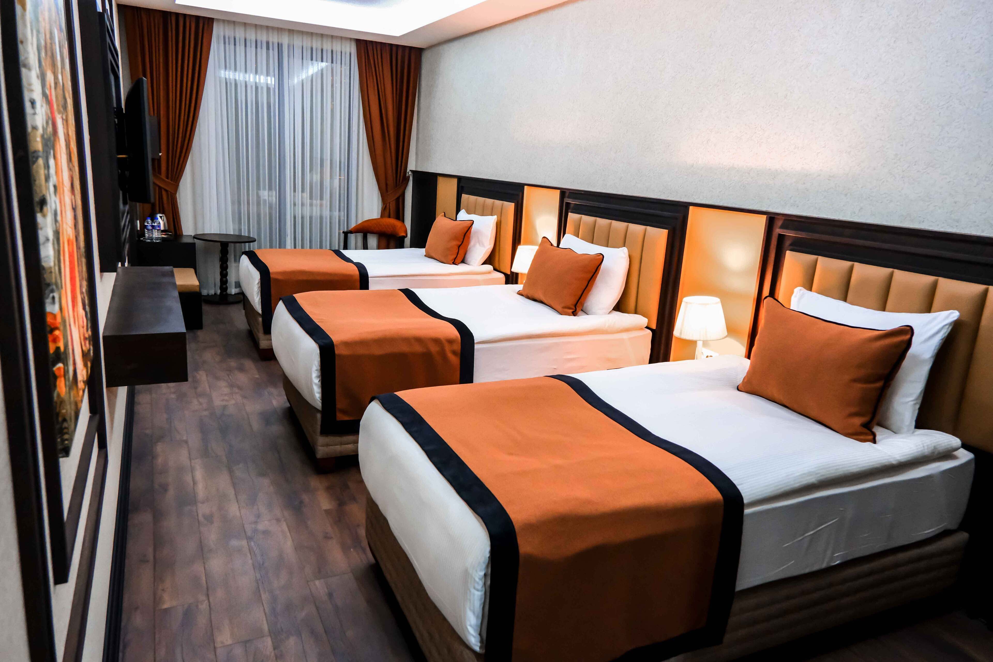 Quarto de hotel com três camas, televisão, uma mesinha e um banquinho.
