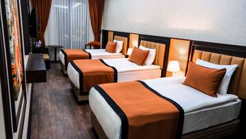 Quarto de hotel com três camas, televisão, uma mesinha e um banquinho.