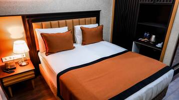 Quarto de hotel com uma cama, uma mesa de cabeceira com abajur e uma pequena mesa com chaleira e garrafas.