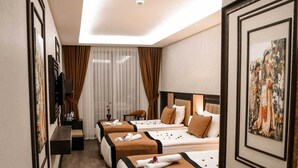 Ein Hotelzimmer mit drei Betten, einem Schreibtisch, einem Stuhl, einem Fernseher und einem großen Fenster mit Vorhängen.