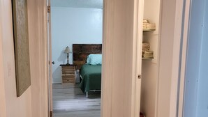 Ein Flur, der in ein Schlafzimmer mit Holzboden, einem Bett mit grüner Bettwäsche und einem Nachttisch mit Lampe führt.