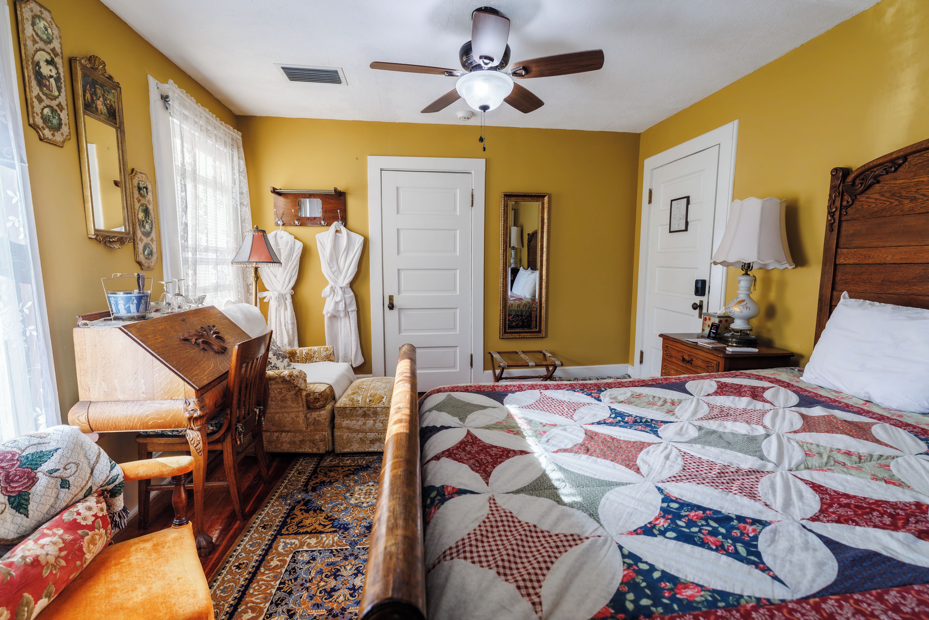 A bedroom with a bed, wooden furniture, a ceiling fan, and a large mirror.