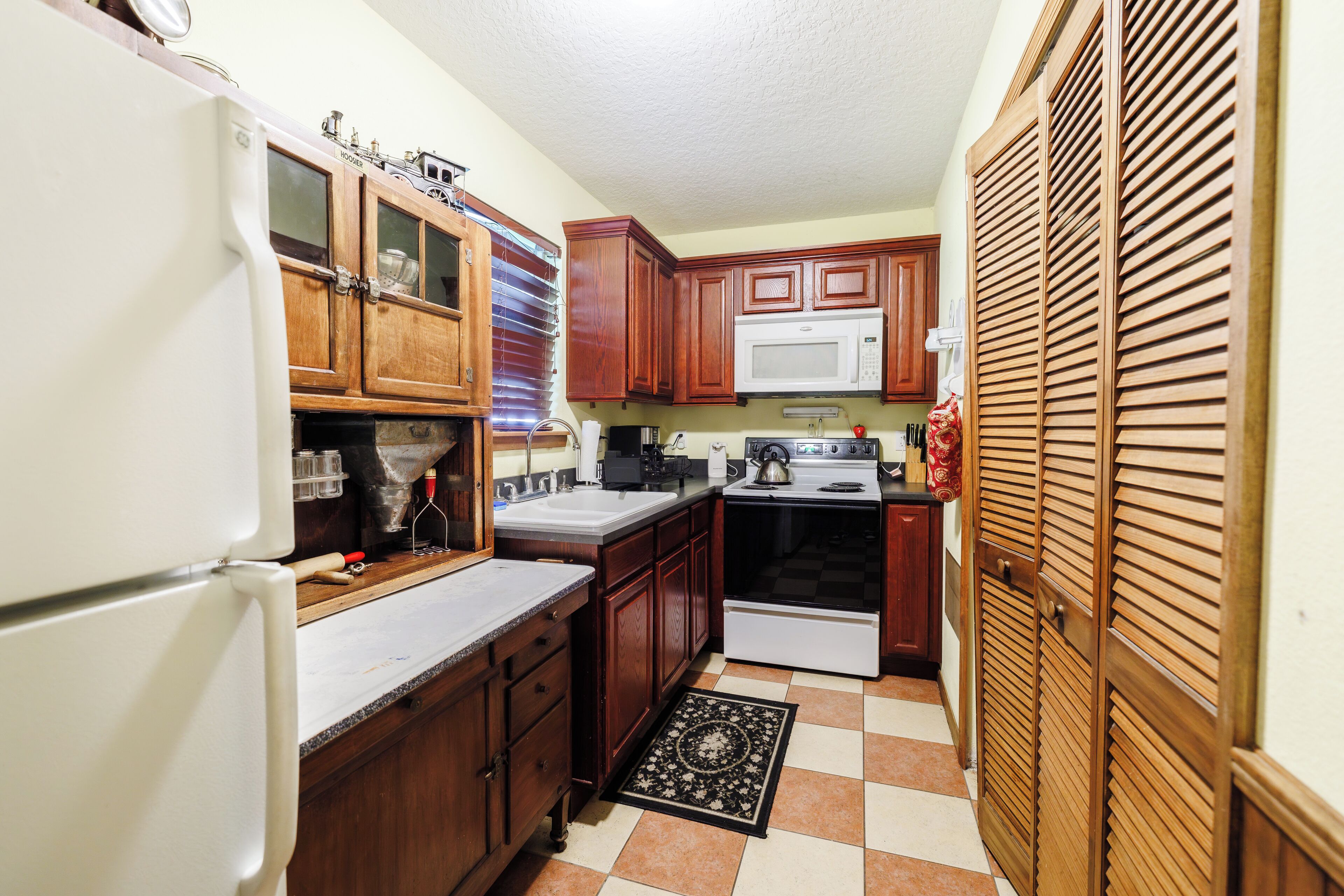 A compact kitchen with wooden cabinets, a white refrigerator, a microwave, and a stove.