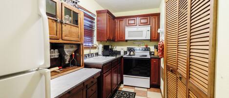 A compact kitchen with wooden cabinets, a white refrigerator, a microwave, and a stove.