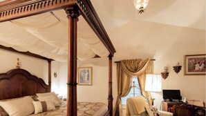 A four-poster bed with a canopy, a chair, a desk with a computer, and a painting on the wall. - Alling House (Orange City)