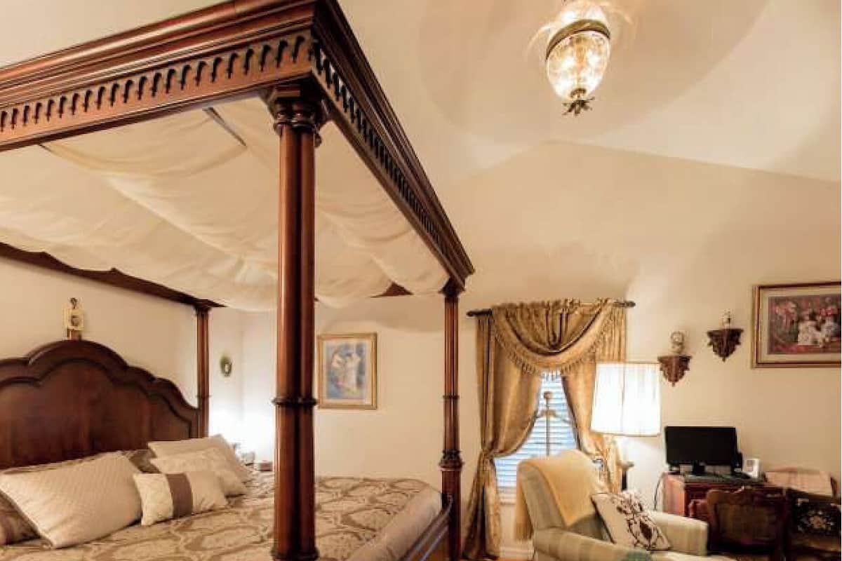 Un lit à baldaquin, une chaise, un bureau avec un ordinateur et un tableau accroché au mur.