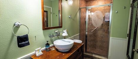 A bathroom with a wooden vanity, a large mirror, a sink, and a shower area.