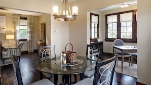 A dining area with a round glass table, chairs, a chandelier, and a window with blinds. - Charming Carnegie Cottage 15 Minutes from Airport & Downtown (Carnegie)