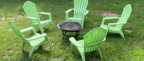 A round table with a fire pit in the center, surrounded by six green plastic chairs.