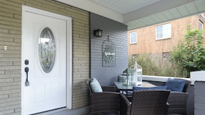 A covered porch with wicker furniture, a white door, and a welcome mat. - Charming Carnegie Cottage 15 Minutes from Airport & Downtown (Carnegie)