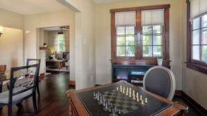 A spacious living room with a large wooden coffee table, a fireplace, and a chessboard set up for play. - Charming Carnegie Cottage 15 Minutes from Airport & Downtown (Carnegie)