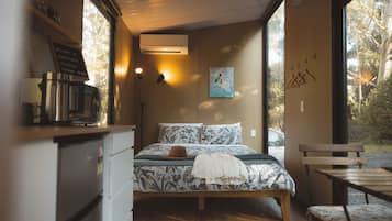 Un dormitorio con cama, escritorio con cafetera, un cuadro en la pared y vistas a árboles a través de la ventana.