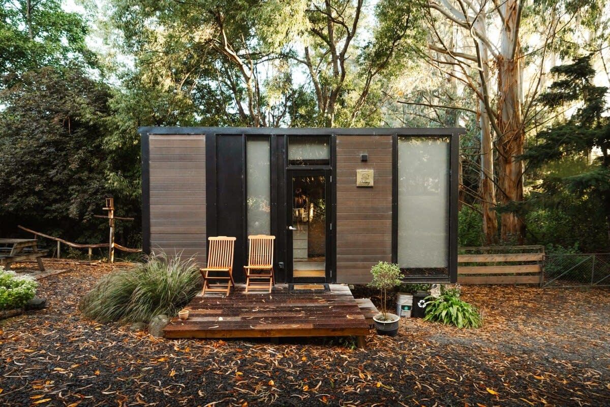 A modern cabin with a wooden deck, two chairs, and a small garden area.