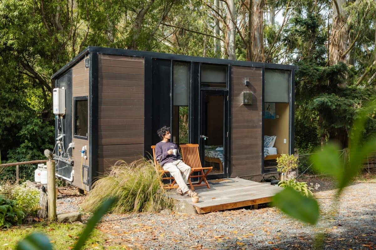 A small cabin with a wooden deck, a single chair, and a bed inside.