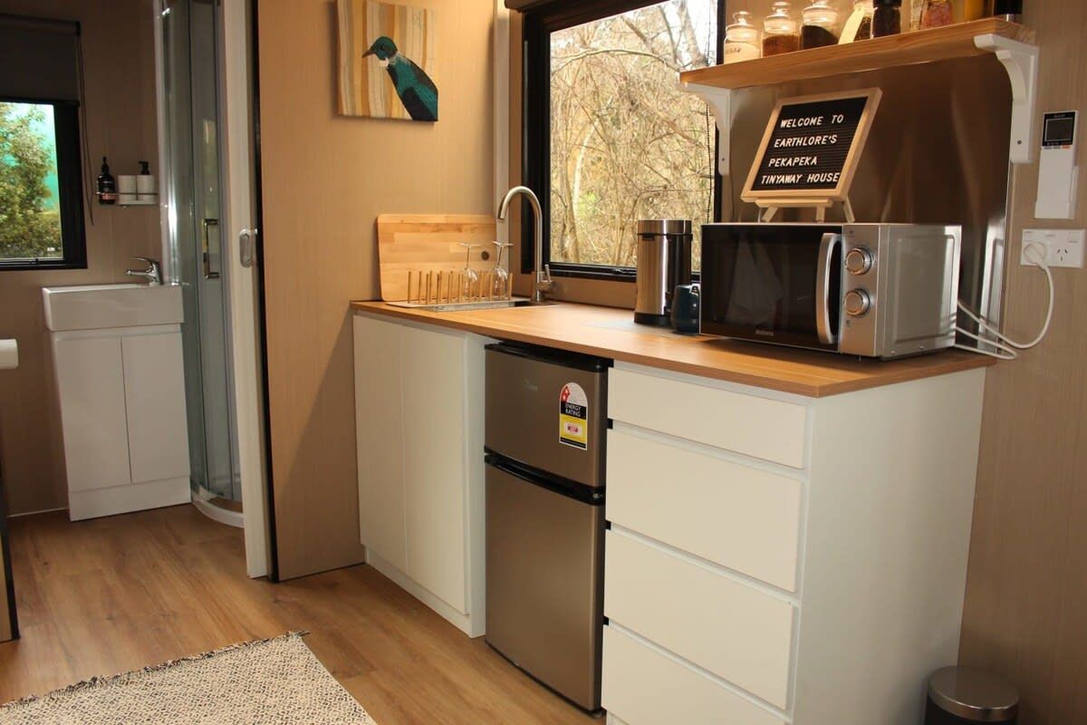 Una cocina compacta con un lavamanos, microondas, refrigerador y tabla de cortar de madera.