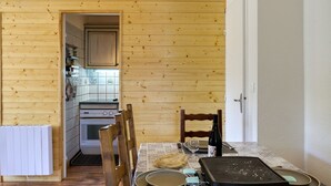 Ett rum med träpanel på väggarna, ett köksområde, ett matbord med stolar och en grill.