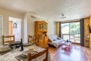 A room with a dining table set for two, a sofa, wooden cabinets, and a large window.