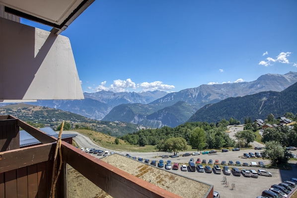 Udsigt til et bjerg fra en balkon med en parkeringsplads og bygninger i forgrunden.