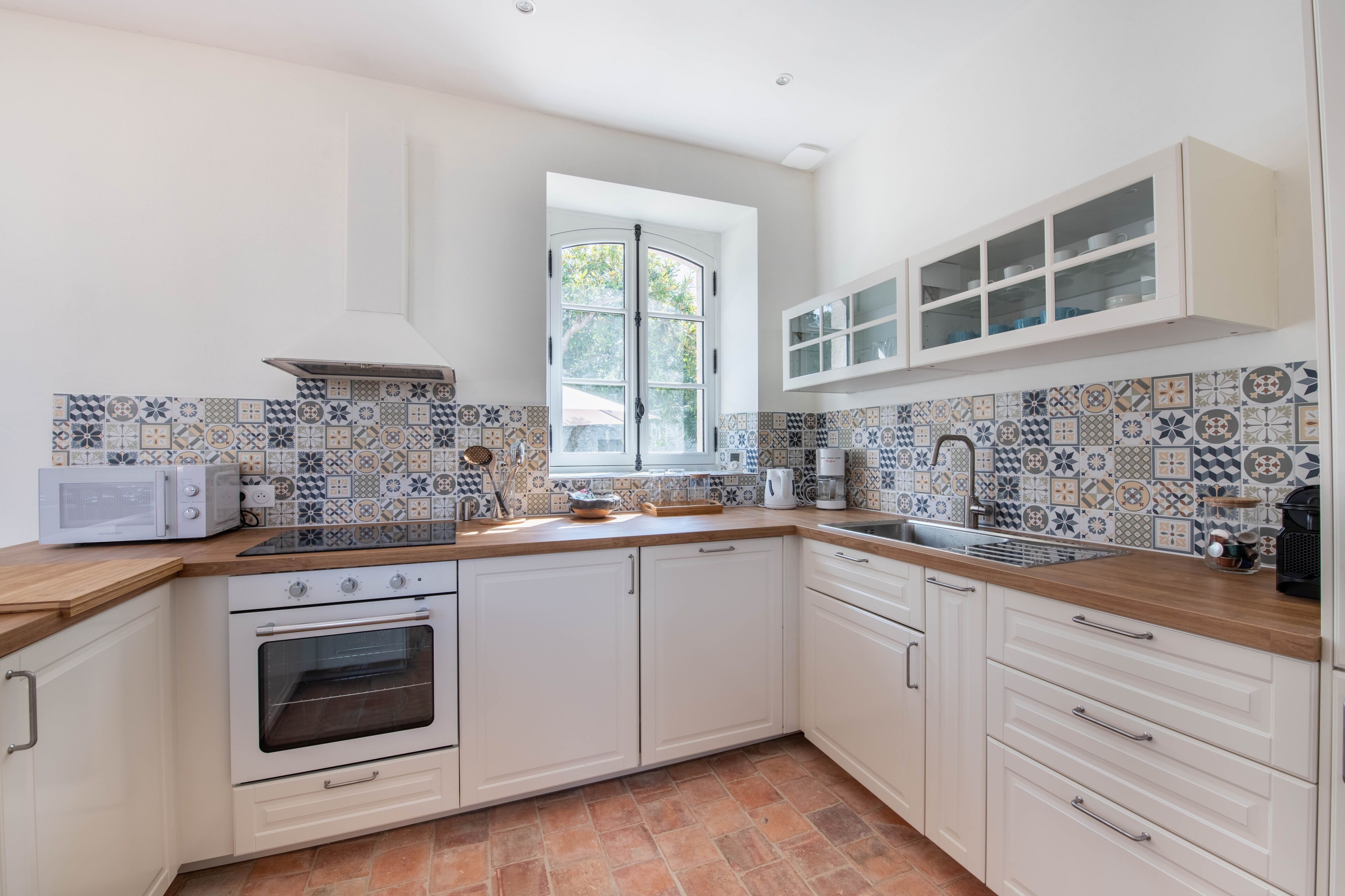 A kitchen with white cabinets, a microwave, an oven, a sink, and a window with a view of greenery.