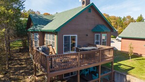 A two-story cabin with a balcony, a covered outdoor seating area, and a garage.