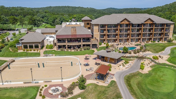 A multi-story hotel with a pool, outdoor seating, and a golf course in the background.
