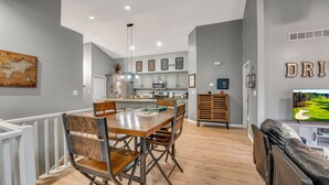 A modern kitchen with grey cabinets, a dining area with wooden chairs, and a TV displaying a golf course.