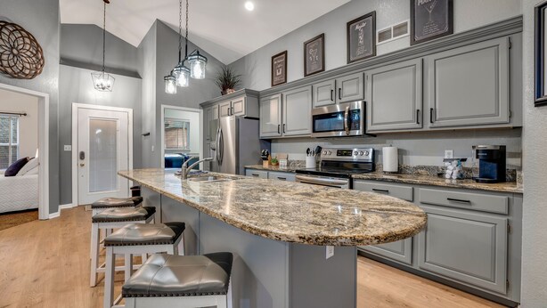 A modern kitchen with granite countertops, stainless steel appliances, and grey cabinetry.
