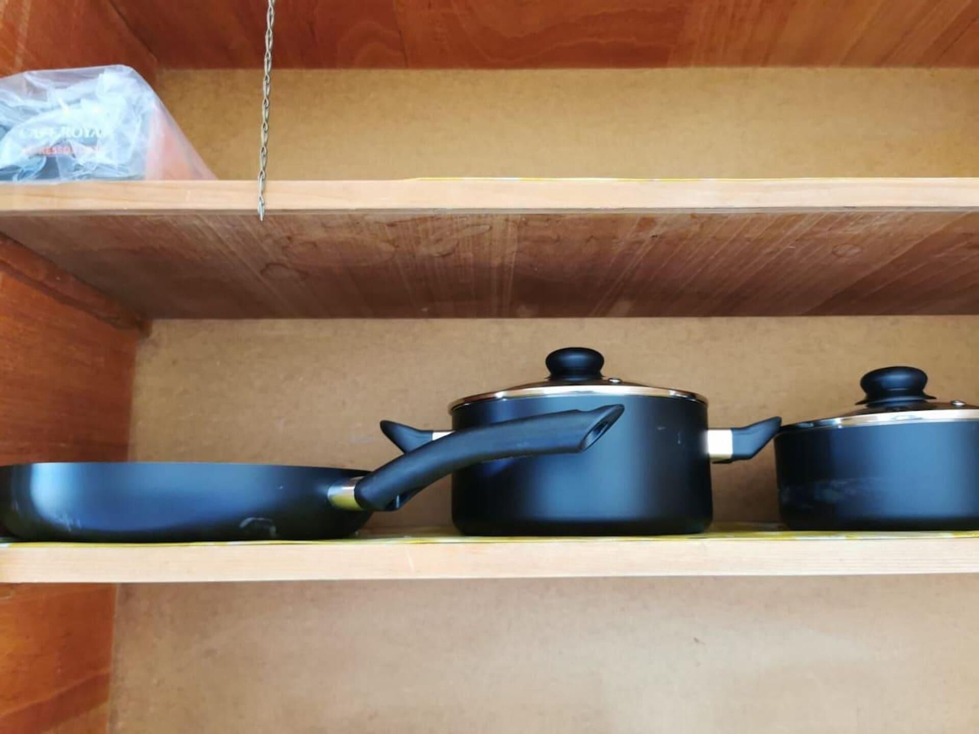 A wooden shelf with two black pots and a pan.