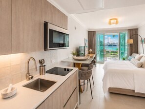 Une chambre d’hôtel moderne équipée d’une kitchenette, d’un lit, d’un bureau et offrant une vue sur l’extérieur.