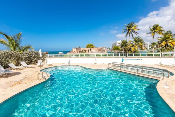 A pool with clear blue water, surrounded by palm trees and a white fence.