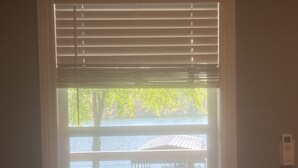 Ein Fenster mit Jalousien, Blick auf einen Steg und ein Gewässer.