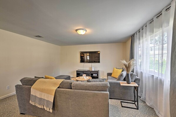 A modern living room with grey sofas, a coffee table, and a flat-screen TV mounted on the wall.