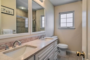 A bathroom with a double sink, a toilet, a large mirror, and a window. - Glen Cove Home: Walk to Boardwalk + Dining! (Glen Cove)