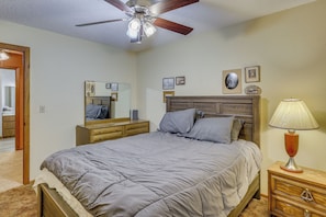 Una camera da letto con un letto, un comodino, una lampada, una ventola a soffitto, una cassettiera, uno specchio e quadri appesi al muro.