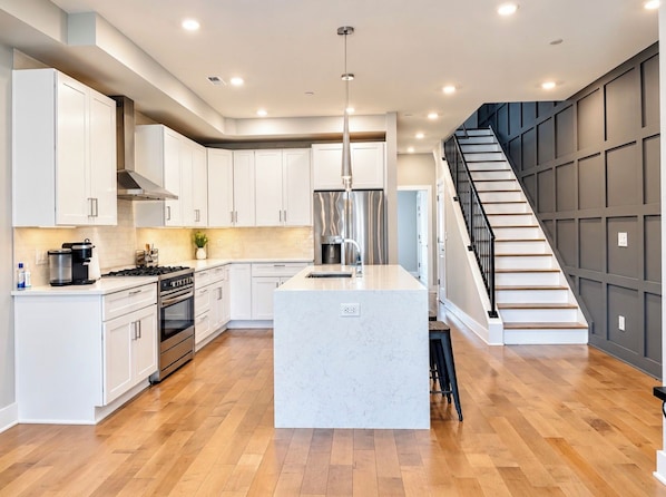 A modern kitchen with white cabinetry, a central island, stainless steel appliances, and a wooden staircase.