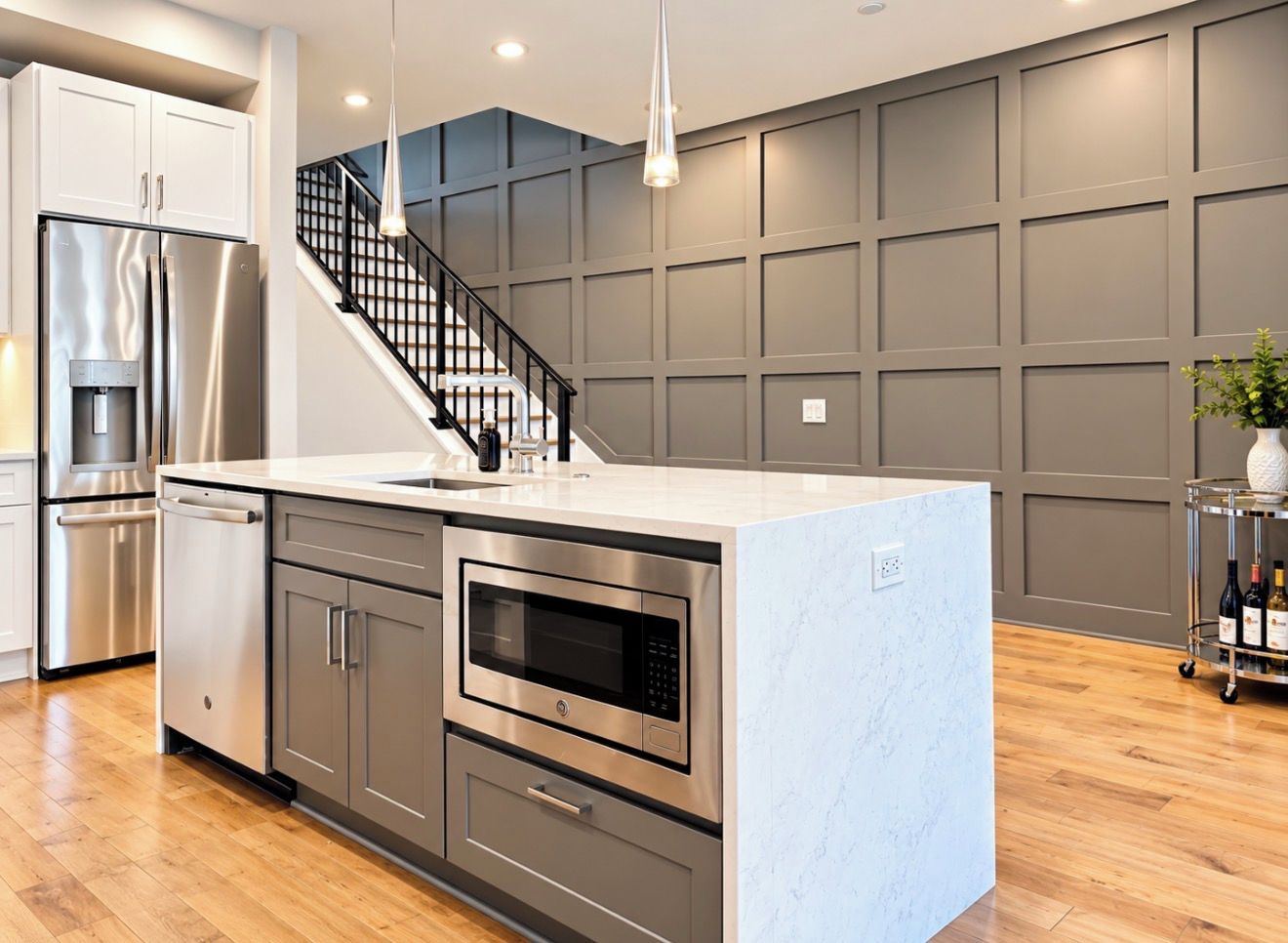 A modern kitchen with stainless steel appliances, a central island, and a staircase leading to an upper level.