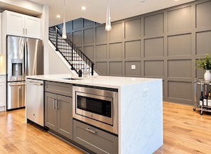 A modern kitchen with stainless steel appliances, a central island, and a staircase leading to an upper level.