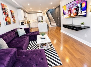 Ein modernes Wohnzimmer mit einem violetten Sofa, einem Couchtisch und einem Flachbildfernseher.