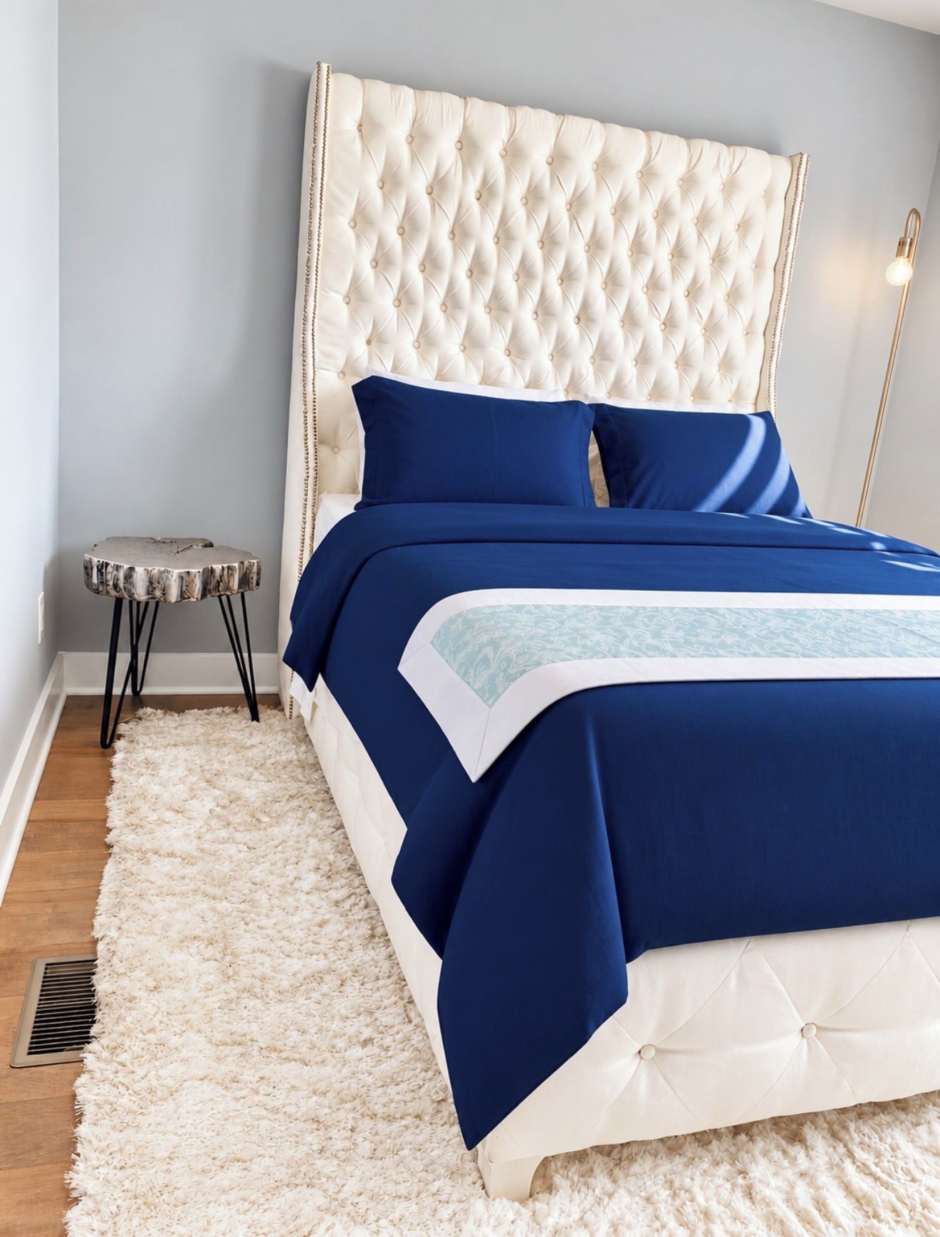 A bedroom with a tufted headboard, a white fluffy rug, and a small side table.