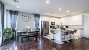 A modern kitchen with white cabinets, stainless steel appliances, and a central island with bar stools. - Inviting Sunny House! Poker table~ 4br 3ba 7 beds/ 10 mins to Airport & Strip! (Las Vegas)