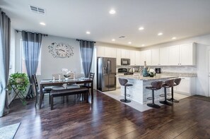 A modern kitchen with white cabinets, stainless steel appliances, and a central island with bar stools. - Inviting Sunny House! Poker table~ 4br 3ba 7 beds/ 10 mins to Airport & Strip! (Las Vegas)