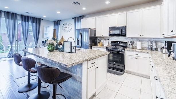 A modern kitchen with white cabinets, a granite countertop, and a large island with bar stools. - Inviting Sunny House! Poker table~ 4br 3ba 7 beds/ 10 mins to Airport & Strip! (Las Vegas)